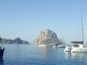 A serene view of multiple yachts anchored near a rocky island, showcasing the beauty of the Mediterranean coastline.