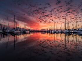 A stunning sunset reflects off the calm waters of a marina filled with yachts, creating a picturesque scene perfect for boat enthusiasts and photographers.