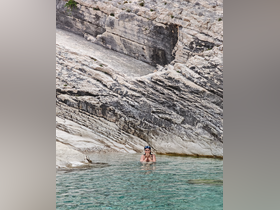A woman enjoys a refreshing swim in crystal-clear waters against a stunning rocky coastline, perfect for adventure seekers and nature lovers.