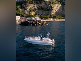 A man stands on a sleek boat, navigating the serene waters with stunning cliffs in the background, perfect for exploring coastal destinations.