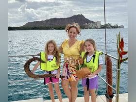 A joyful family moment aboard a boat, featuring two children in life vests holding unique items against a stunning backdrop of Diamond Head in Hawaii.