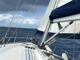 A close-up view of a sailboat's deck as it navigates through open waters, showcasing the rigging and sails against a dramatic sky.