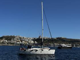 A picturesque view of a sailboat anchored in calm waters, with a scenic coastal backdrop showcasing residential buildings and hills — ideal for sailing enthusiasts and coastal exploration.
