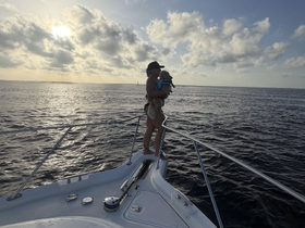 A child enjoys a scenic moment on the bow of a boat, holding a dog against the backdrop of a beautiful sunset over the ocean — a perfect family adventure on the water.