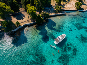 Aerial view of a boat anchored in crystal-clear turquoise waters, with two swimmers enjoying the sun — a perfect scene for summer adventures and relaxation.