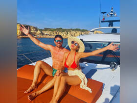A joyful couple relaxes on the deck of a yacht, enjoying the sun and stunning coastal views — perfect for a romantic getaway or celebration on the water.