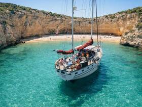 A beautiful sailing vessel anchored near a secluded beach, with guests enjoying the stunning turquoise waters and scenic cliffs — perfect for a day of relaxation and exploration.