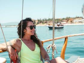 A woman enjoys a sunny day on a sailboat, smiling and relaxing while surrounded by beautiful waters — a perfect moment for sailing enthusiasts.