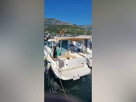 A well-maintained Jeanneau boat docked in a marina, showcasing its sleek design against a backdrop of lush mountains.
