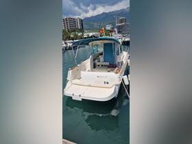 A pristine Jeanneau boat docked in a marina, showcasing its sleek design against a backdrop of mountains and modern buildings.