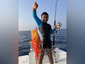 A young boy proudly displays his catch of colorful fish while fishing on a boat in the ocean — a memorable moment for any fishing adventure.
