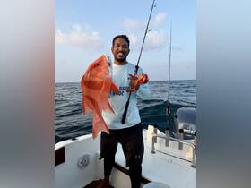 A proud angler displays a vibrant red snapper while fishing on a boat, showcasing the thrill of a successful catch in open waters.