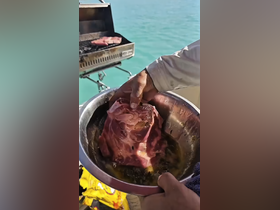 A close-up of a hand holding marinated meat in a bowl, with a grill in the background, showcasing the culinary delights of a boat barbecue experience.