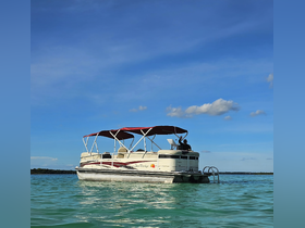 A pontoon boat glides through clear waters with a person waving from the deck, capturing the essence of a fun day on the water.