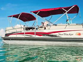 A stylish Sun Tracker pontoon boat, named 'Pamela Anderson', is docked in clear waters, showcasing its sleek design and vibrant colors — perfect for leisurely outings on the water.
