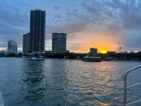 A serene sunset view over the water featuring a boat anchored near the shore, with city buildings in the background — perfect for capturing the beauty of evening cruises.