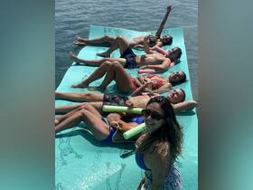 A lively group enjoys sunbathing and relaxing on a floating mat in the water, showcasing the perfect summer day on the water.