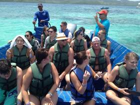 A lively group of guests wearing life jackets enjoys a boat ride in clear turquoise waters, perfect for adventure and exploration.