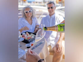 A couple enjoys a celebratory moment aboard a yacht, pouring champagne and savoring delicious sushi — perfect for romantic getaways or special occasions on the water.