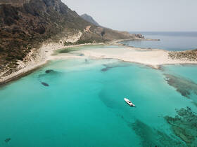 A stunning aerial view of a boat anchored in crystal-clear turquoise waters, surrounded by a picturesque beach and rocky coastline — an ideal destination for relaxation and exploration.