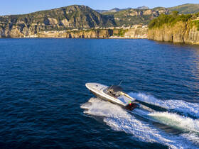 A stunning aerial view of a sleek speedboat cruising through the vibrant blue waters, showcasing the beautiful coastal scenery in the background.