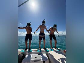 Three excited kids prepare to snorkel off the side of a boat, showcasing the thrill of aquatic adventures on a sunny day.