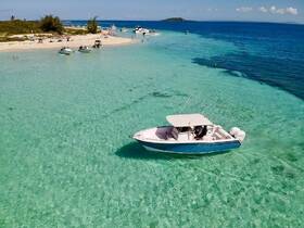 A scenic view of a boat navigating through crystal-clear waters near a sandy beach, showcasing a vibrant sandbar experience perfect for island hopping and relaxation.