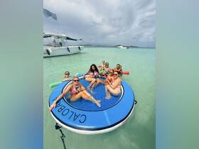 A lively group of friends enjoys a fun day on a floating mat in crystal-clear waters, perfect for relaxation and celebration under the sun.