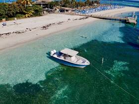 A beautiful aerial view of a pontoon boat anchored near a sandy beach, with guests enjoying the clear waters — perfect for a relaxing day at the sandbar.