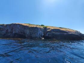 A stunning view of a rocky coastline under a clear blue sky, showcasing the natural beauty of the area — perfect for eco tours or scenic boat trips.
