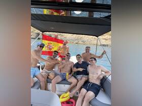 A lively group of friends enjoys a summer day on the boat, celebrating with drinks and laughter while showcasing the Spanish flag — perfect for memorable outings on the water.