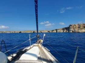 A scenic view from the front of a sailboat navigating through clear blue waters, with rocky cliffs in the background — perfect for sailing enthusiasts and coastal explorations.