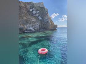 A colorful inflatable donut float rests in the crystal-clear waters near a rocky cliff, perfect for a relaxing day on the water.
