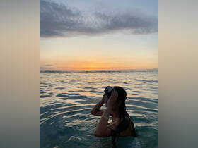 A woman enjoys a serene sunset swim in the ocean, capturing the beauty of the moment as the sun dips below the horizon — an ideal scene for sunset lovers and beachgoers.