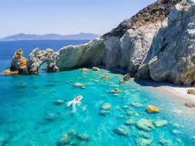 A stunning view of a person kayaking in crystal-clear waters near a rocky arch, showcasing the beauty of the coastline and inviting adventure seekers to explore.