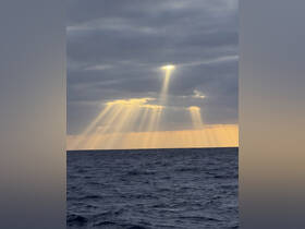 A breathtaking view of sunlight breaking through the clouds over the ocean, creating a stunning display of rays — perfect for capturing the beauty of nature during a boat trip.
