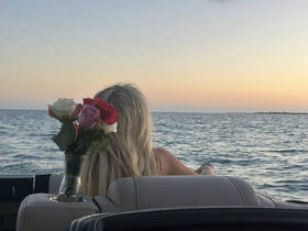 A woman enjoys a serene sunset on a boat, with a bouquet of roses beside her, creating a romantic atmosphere perfect for special occasions.