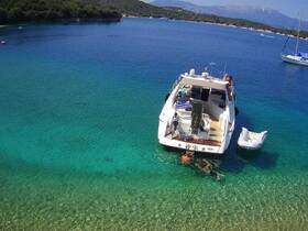 A group enjoys a refreshing swim near their boat in crystal-clear waters, showcasing the perfect summer getaway in a picturesque bay.