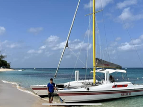 A person stands beside a catamaran on the beach, showcasing a perfect day for sailing and relaxation by the water.