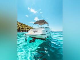 A stunning view of a Leader 605 boat anchored in crystal-clear turquoise waters, surrounded by lush greenery — perfect for summer adventures on the water.