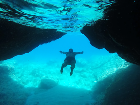 A swimmer explores the vibrant underwater world beneath a rocky arch, showcasing the beauty of marine life and crystal-clear waters — perfect for adventure seekers.