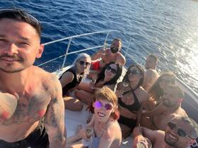 A lively group enjoys a fun day on a yacht, celebrating with cocktails and smiles against the backdrop of sparkling blue waters.
