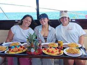 Three friends enjoy a delicious meal aboard a boat, featuring vibrant dishes and refreshing drinks — perfect for a memorable dining experience on the water.