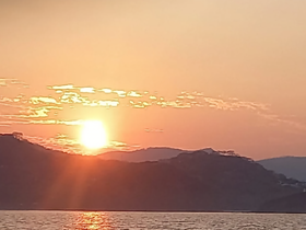 A stunning sunset over the coastline, casting a warm glow on the water — a perfect backdrop for evening boat cruises.