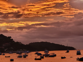 A stunning sunset casts vibrant colors over a bay filled with boats, creating a picturesque scene perfect for evening cruises and coastal adventures.