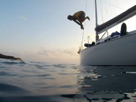 A person leaps off the side of a sailboat into the water at sunset, capturing the thrill of on-water adventures and the joy of sailing.