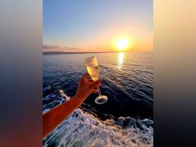 A hand raises a glass of champagne against a stunning sunset backdrop, capturing the essence of celebration aboard a boat — perfect for romantic evenings or special occasions on the water.