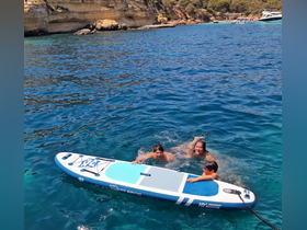 A family enjoys a fun day in the water, swimming and paddleboarding together in a beautiful coastal setting — perfect for summer adventures.