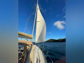 A stunning view of a sailboat underway, showcasing its white sails against a clear blue sky and lush green hills in the background — perfect for sailing enthusiasts.