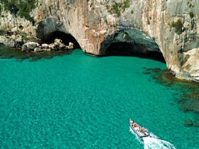 A scenic view of a boat navigating through turquoise waters near stunning coastal caves, perfect for adventure seekers exploring hidden gems.
